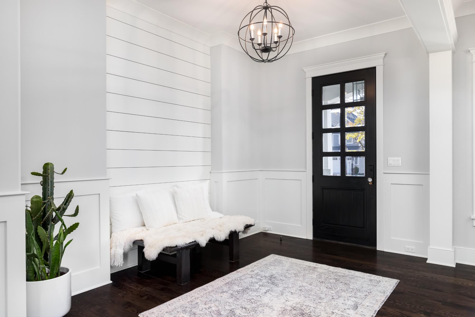 a-beautiful-foyer-entrance-with-a-light-hanging-above-the-dark-hardwood-floors-a-bench-in-front-of-a-shiplap-wall-and-a-dark-door-with-windows