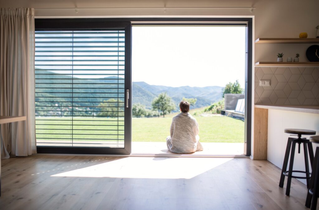 A rear view of young woman sitting by patio door at home. Copy space.