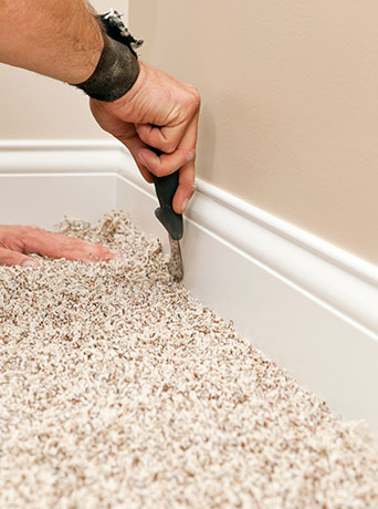 man using tool to install carpet along baseboards