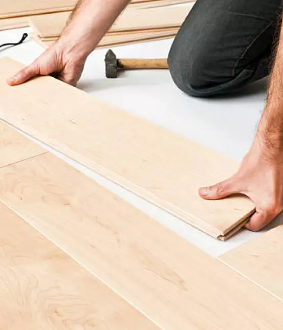 Man installing flooring with hammer laying beside him