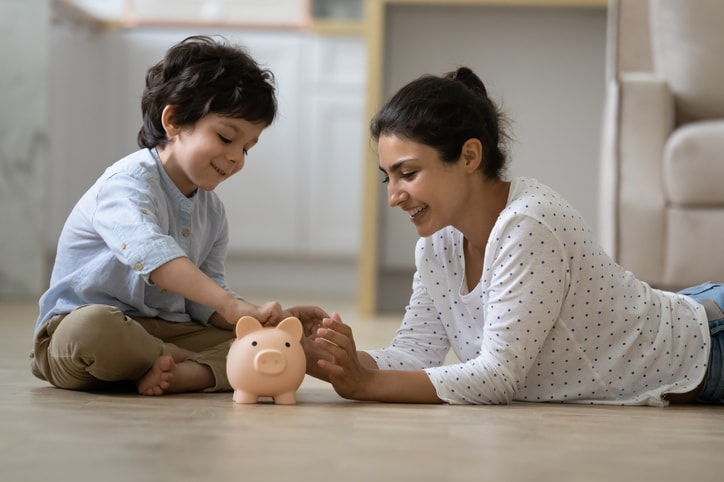 mother and child sitting on floor looking at piggy bank