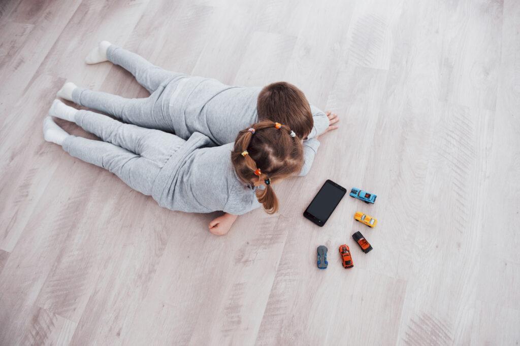 Top view. Children using digital gadgets at home. Brother and sister on pajamas watch cartoons and play games on their technology tablet.