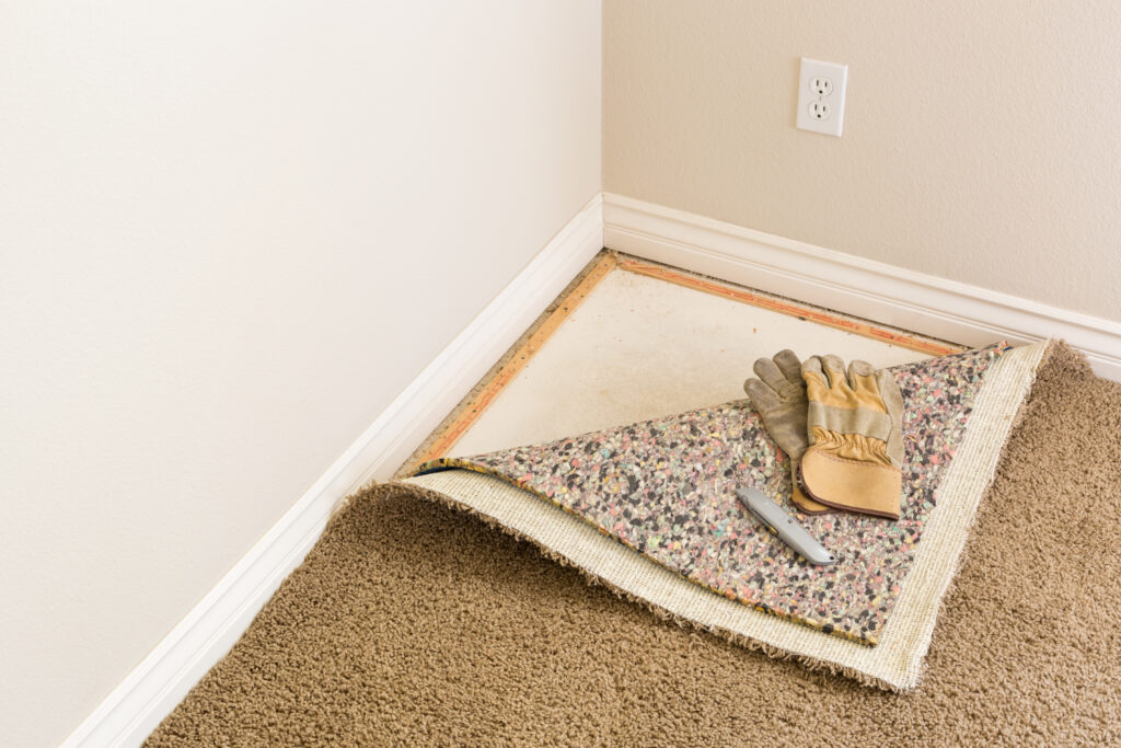 Construction Gloves and Utility Knife On Pulled Back Carpet and Pad In Room.