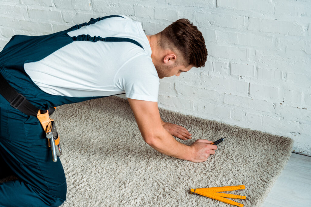 installer in overalls holding cutter near carpet