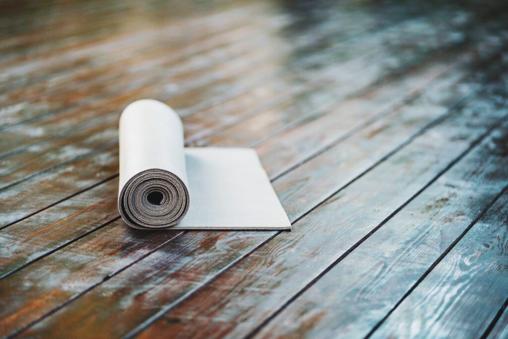 rolled-yoga-mat-on-wooden-deck-background-fitness-2023-11-27-05-22-33-utc