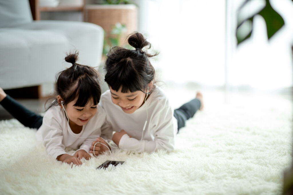 Asian Siblings together on the floor using smartphone