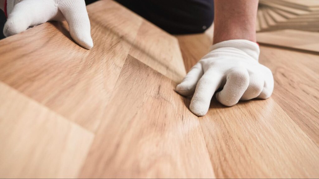 installing-laminated-floor-detail-on-man-hands-in-white-gloves-fitting-wooden-tiles